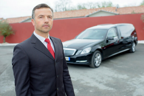 Funeral director in front of funeral cars