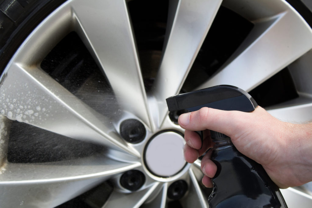 A person wearing gloves cleans a car’s rim.