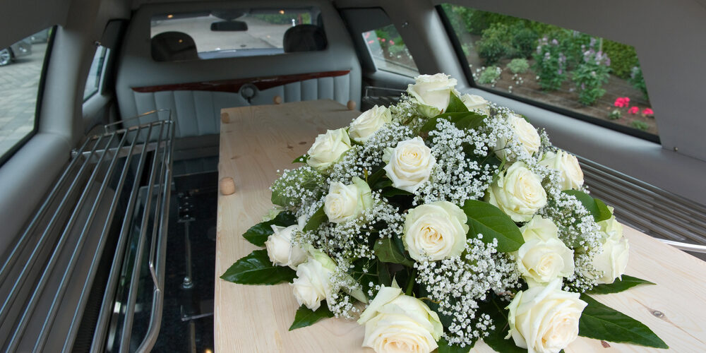 A,Coffin,In,A,Mourning,Car,With,A,Flower,Arrangement Inside of a Funeral Car with Flowers on a Wood Casket