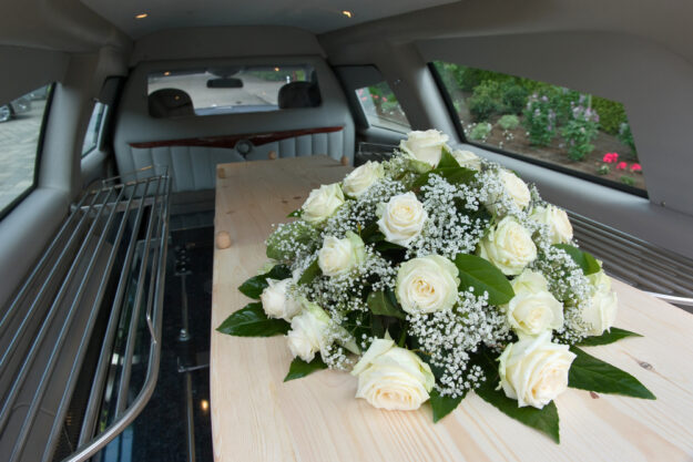 A,Coffin,In,A,Mourning,Car,With,A,Flower,Arrangement Inside of a Funeral Car with Flowers on a Wood Casket