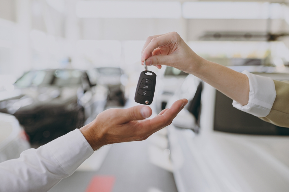Person handing car keys to a buyer inside a funeral vehicle showroom