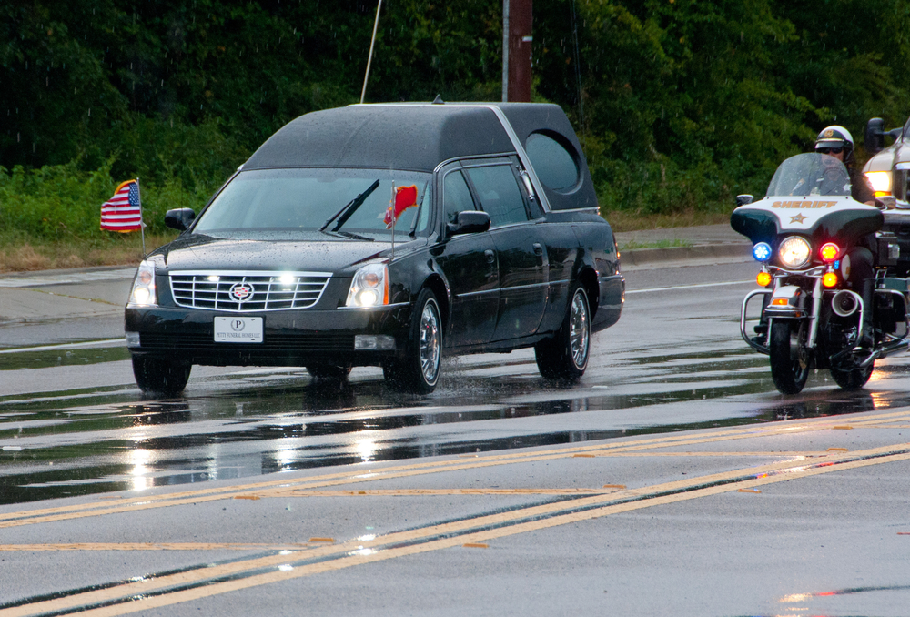 Cadillac hearse in a funeral procession escorted by sheriff motorcycles