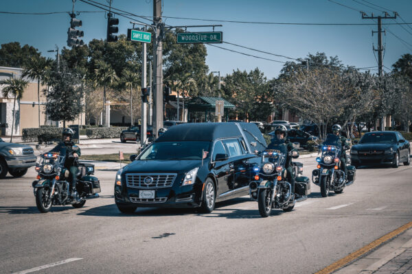 Cadillac hearse leading a funeral procession escorted by police motorcycles in California