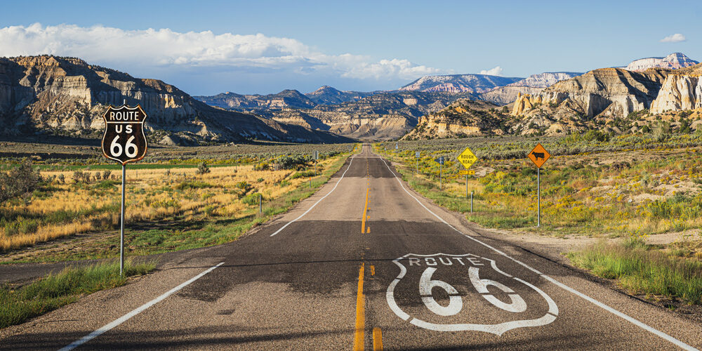 A long stretch of Route 66 runs through the mountains with a large historic highway marker.