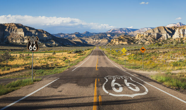Scenic,Panoramic,View,Of,Long,Straight,Road,On,Famous,Route A long stretch of Route 66 runs through the mountains with a large historic highway marker.