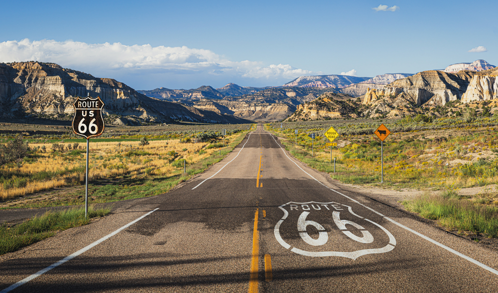 Scenic,Panoramic,View,Of,Long,Straight,Road,On,Famous,Route A long stretch of Route 66 runs through the mountains with a large historic highway marker.