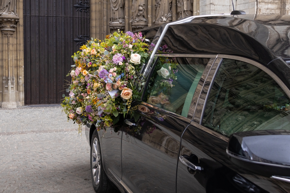 Black funeral car with colorful flower arrangement parked outside a church entrance Black funeral car with colorful flower arrangement parked outside a church entrance