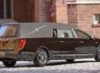 Cadillac funeral hearse with extended roofline and chrome trim parked outside a brick building