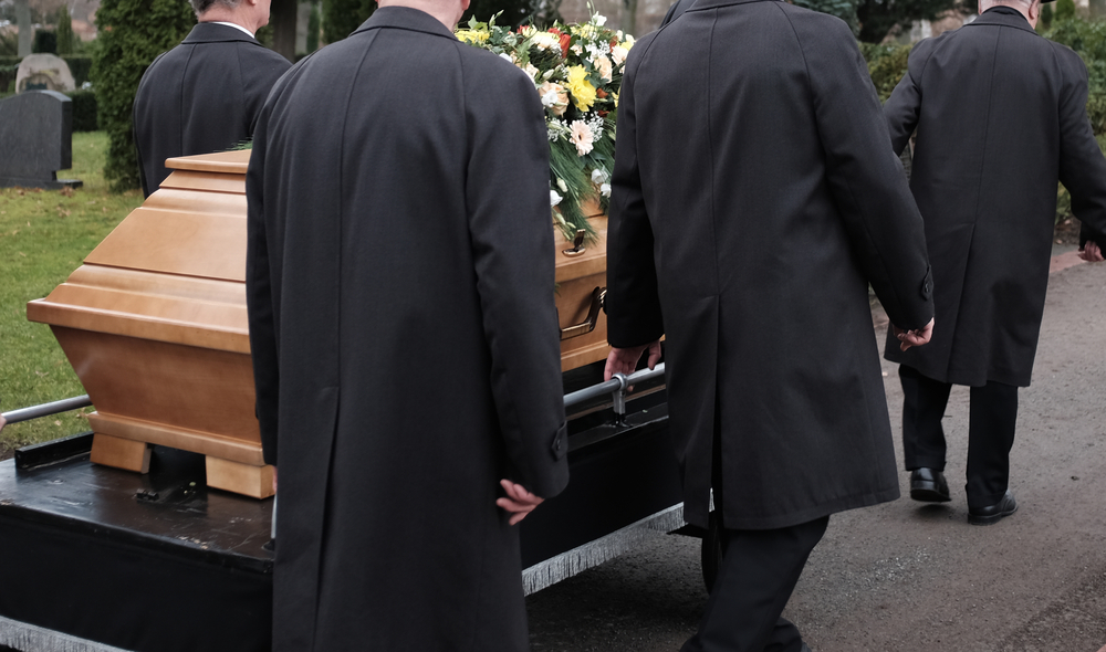 Funeral service with pallbearers transporting a coffin adorned with flowers at a cemetery Funeral service with pallbearers transporting a coffin adorned with flowers at a cemetery