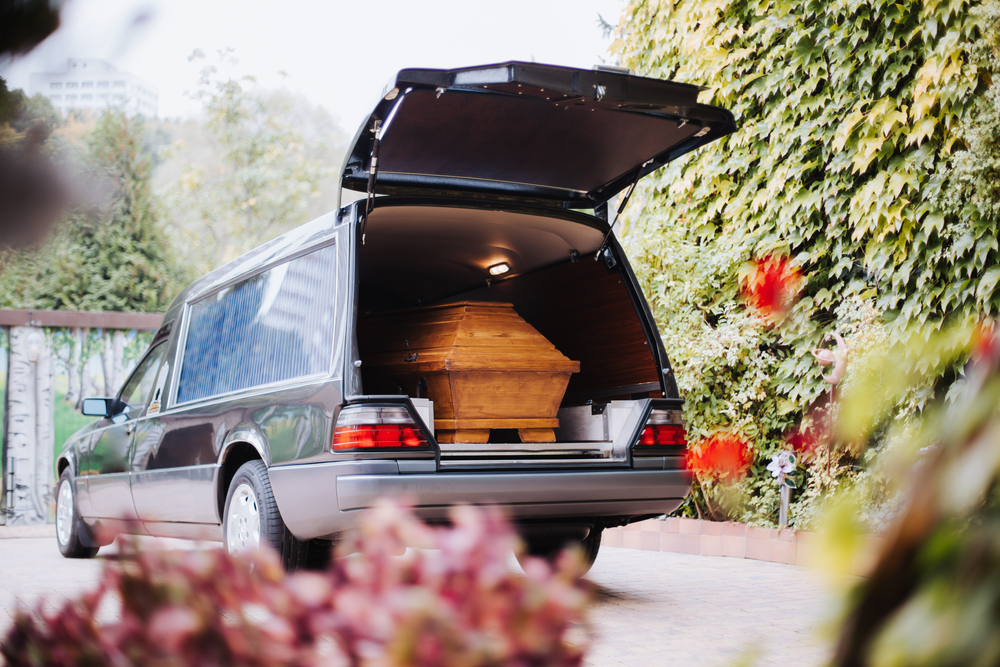 Luxury funeral car transporting a wooden coffin, shown with rear hatch open during a funeral service Luxury funeral car transporting a wooden coffin, shown with rear hatch open during a funeral service