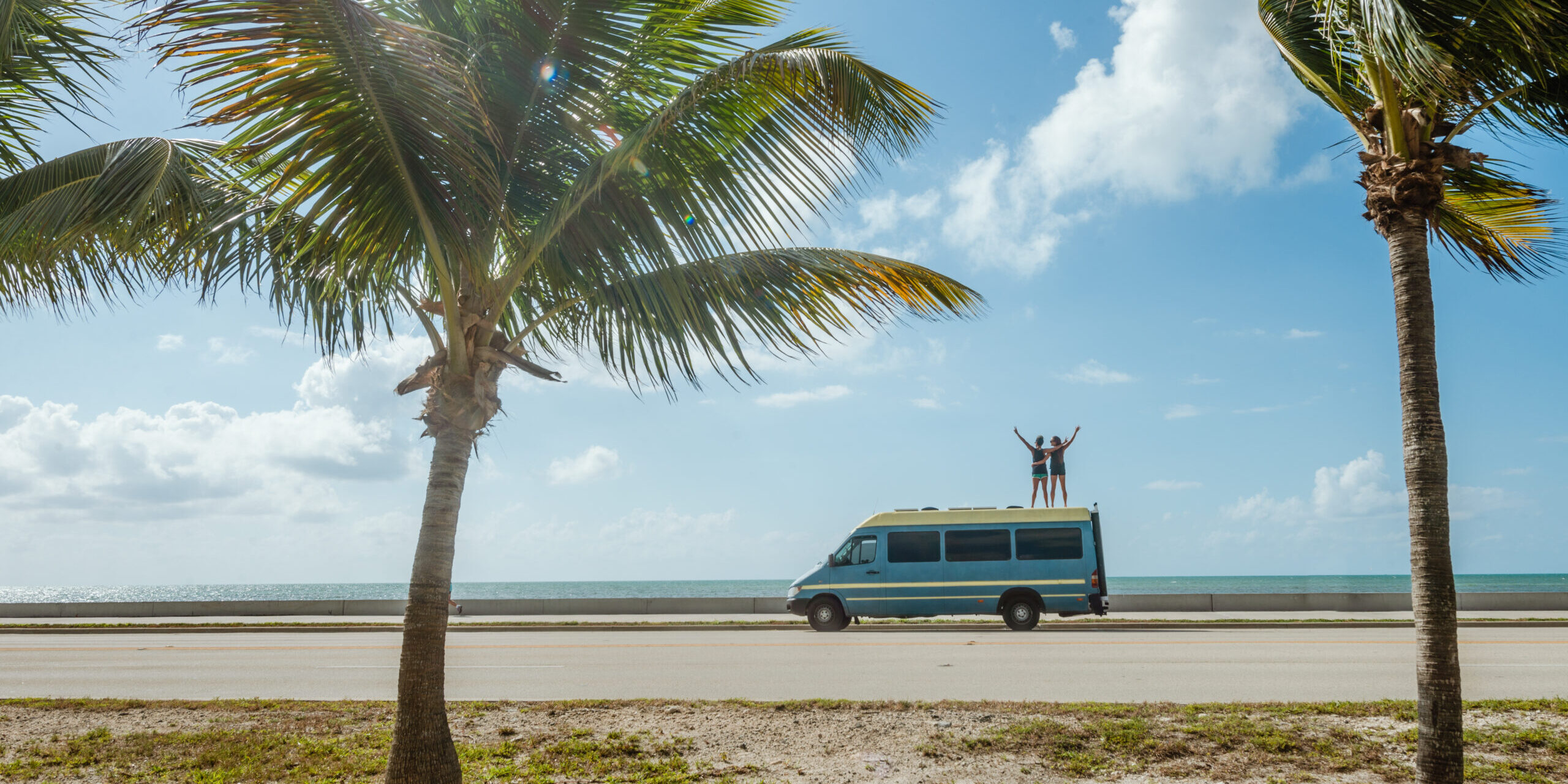 Couple on top of a customized Sprinter van in a tropical setting