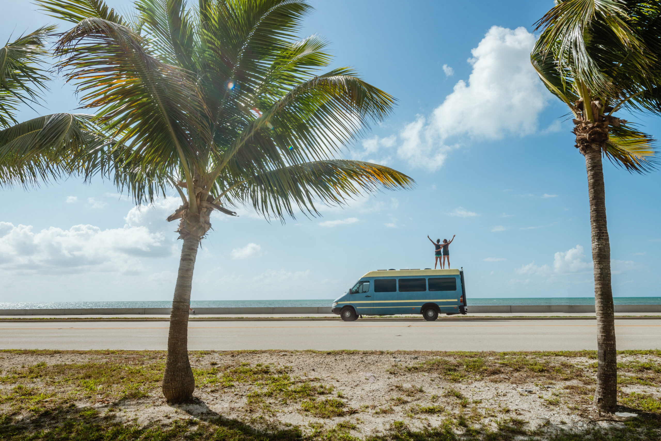Couple on top of a customized Sprinter van in a tropical setting
