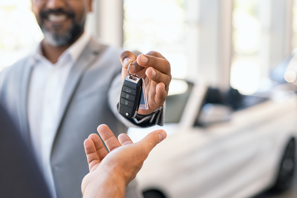 Luxury vehicle salesman handing the key to a customer Luxury vehicle salesman handing the key to a customer