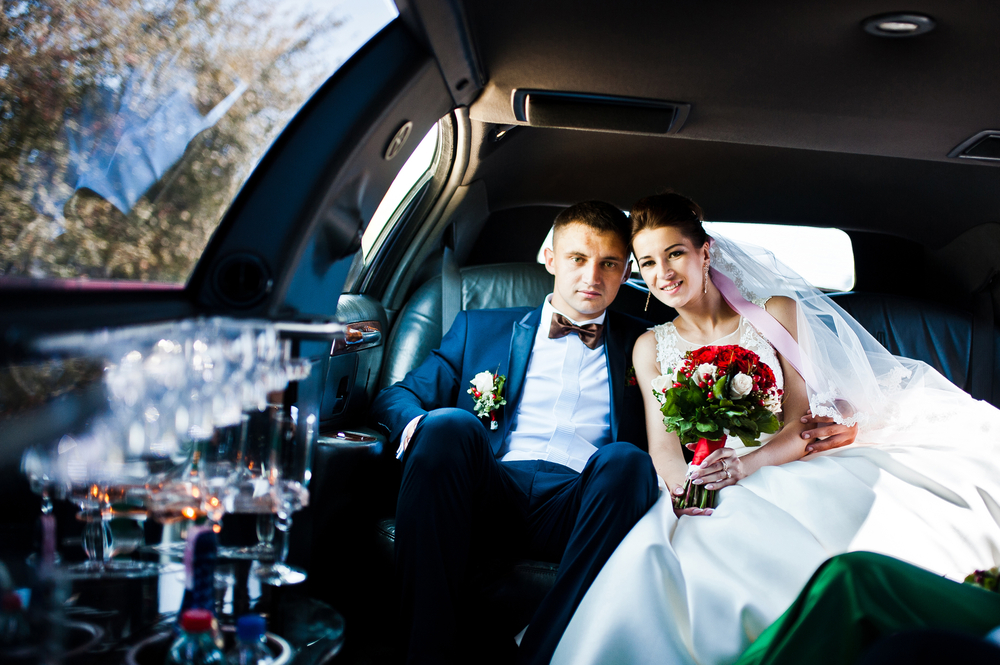 Bride and groom sitting inside a luxury limousine with a flower bouquet