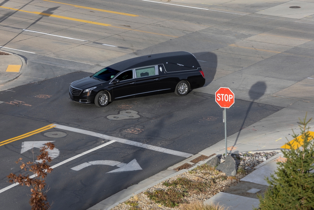 Black funeral hearse driving through a city intersection near a stop sign