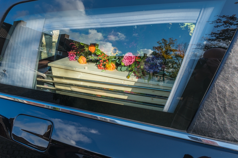 Hearse carrying a light-colored coffin decorated with colorful flowers